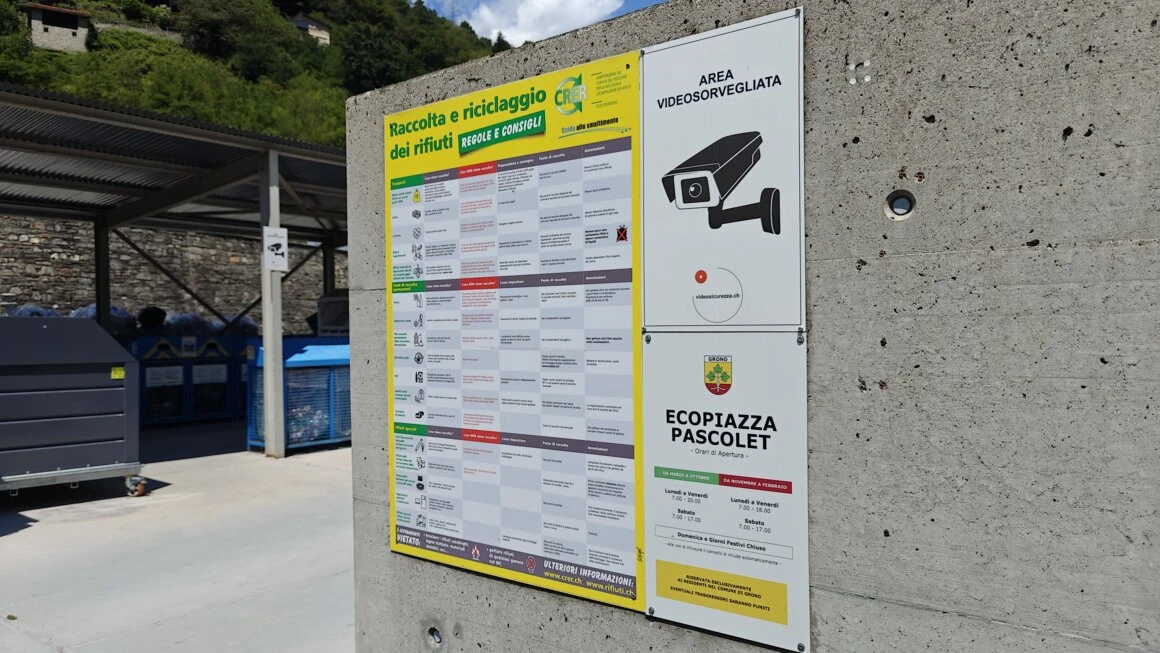 Segnaletica di raccolta rifiuti e cartello area videosorvegliata all’ingresso dell’Ecopiazza Pascolet, con contenitori per il riciclaggio sullo sfondo