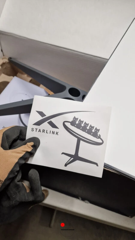 Persona con guanti tiene adesivo Starlink durante apertura del kit di installazione satellitare