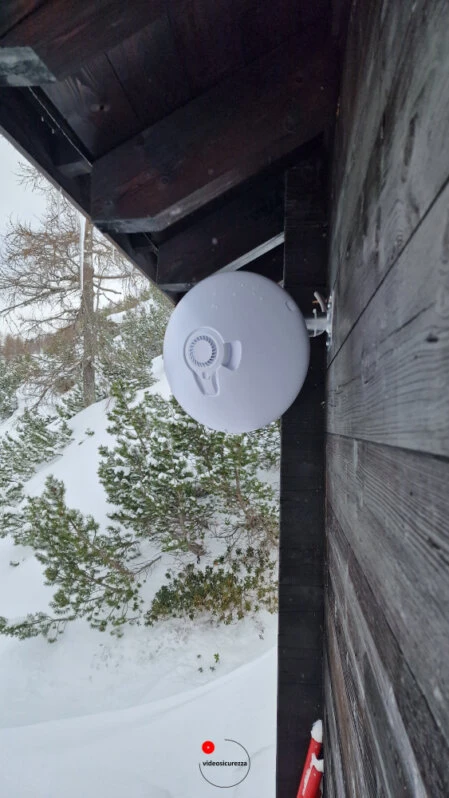 Access point wireless montato su parete in legno di baita alpina, con sfondo innevato e alberi in ambiente montano