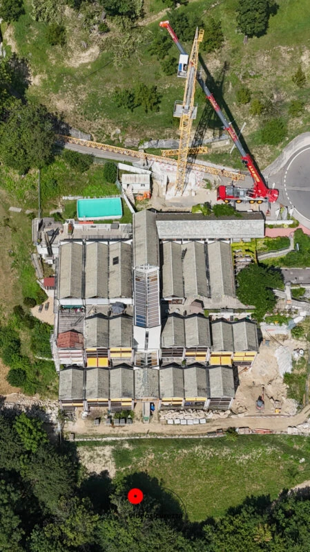 Immagine aerea scattata con drone che mostra un grande edificio industriale con gru e mezzi da cantiere durante lavori di ristrutturazione